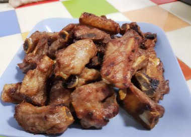 Masada bir tabak tavuk kanadı fotoğrafı, renkli bir masa örtüsünde pişmiş et ve arka planda bir köpek..