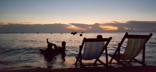 日落时坐在水里的两张椅子 在海滩上折叠椅 一只狗在水里 — 图库照片