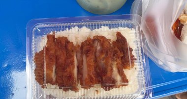 Üzerinde domuz pastırması ve pirinç olan plastik bir konteynırın fotoğrafı mavi bir masada plastik bir kutuda rulo köfteler..