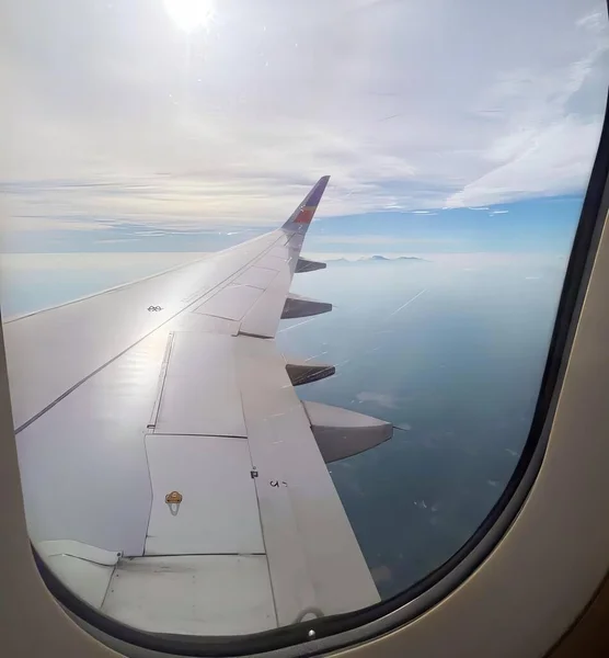 窓からの飛行機の翼の写真です 飛行機の翼が海と太陽を飛んでいます — ストック写真