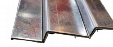 Üzerinde delik olan metal bir şeridin fotoğrafçılığı, kiremit çatı malzemeleri beyaz bir yüzey üzerinde sıralanır..