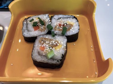 Üzerinde suşi olan sarı bir tepsi, üzerinde dört parça suşi olan bir tepsi..