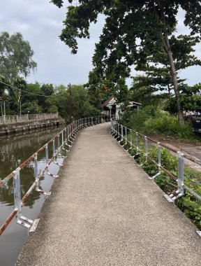 Nehrin üzerinde bir köprü, üzerinde bir köprü ve nehrin yanında bir tekne olan bir yürüyüş yolunun fotoğrafı..