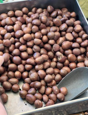 Tavadan fındık toplayan bir kişinin fotoğrafı, at kestaneleri bir spatulayla tavada kızartılıyor..