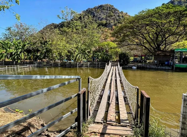 a photography of a bridge over a river with a mountain in the background, boathouse on a river with a wooden bridge over it.