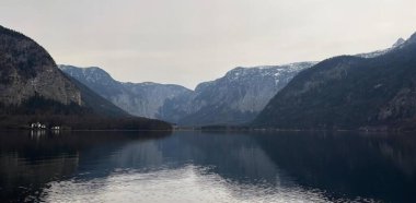 Arka planda dağlar olan bir gölün, dağlarla kaplı bir vadinin ve içinde bir tekne olan bir su kütlesinin fotoğrafı..
