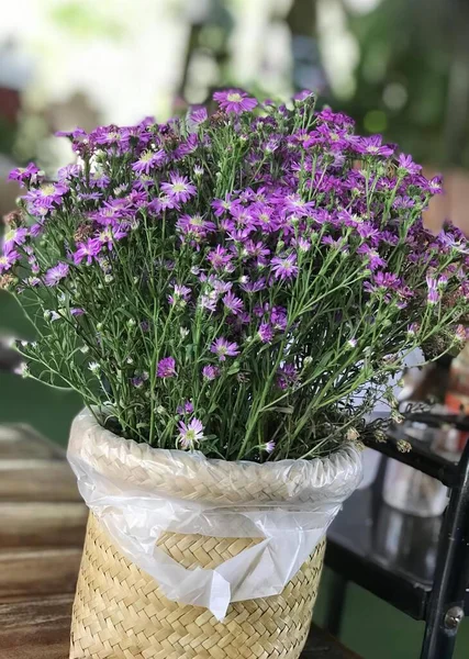 a photography of a basket of purple flowers on a table, flowerpot with purple flowers in a wicker basket on a table.