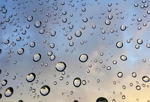a photography of a window with rain drops on it, bubbles of water are seen on a window glass as the sun sets.