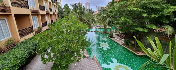 a photography of a pool in a hotel with a wooden deck, there is a small pool in the middle of a building.