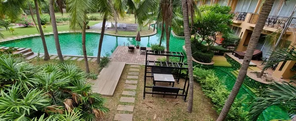 a photography of a pool and a patio with a table and chairs, there is a pool and a patio in the middle of a garden.