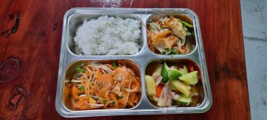Pirinç, sebze ve et içeren dört bölmeli metal bir tepsinin fotoğrafı..