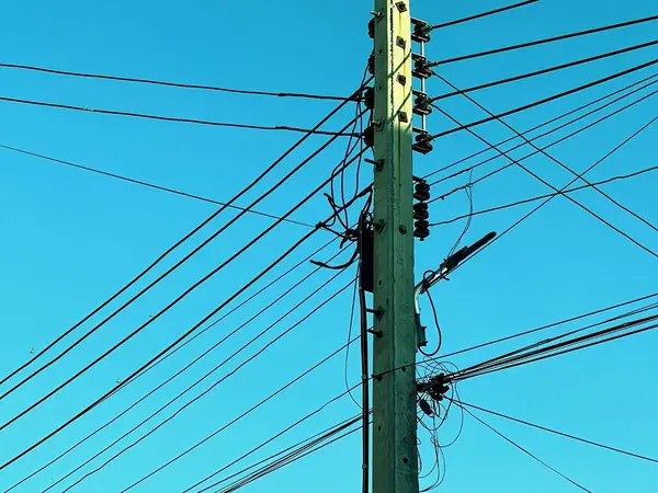 Birçok kablosu ve mavi gökyüzü olan bir telefon direğinin fotoğrafı..