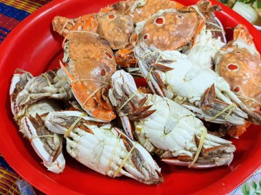 Masadaki yengeçlerle dolu kırmızı bir tabağın fotoğrafı..