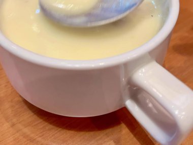 Bir kaşık dolusu sıvının fotografı bir bardağın üzerinde duruyor..