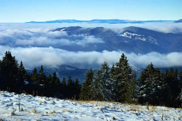 An epic ocean of clouds and fog in the winter mountains landscape, aerial view. Huge white clouds come in waves over the foggy valleys, mountain peaks rise over like islands. Dramatic overcast sky.