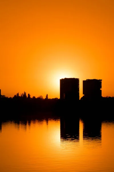 Modern buildings reflected in the calm waters of the lake, bathed in the warm light of the sunrise. High buildings skyscrapers over lake surface. Sunset beautiful cityscape panorama, warm sun light