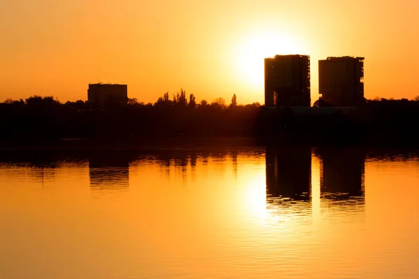 Modern buildings reflected in the calm waters of the lake, bathed in the warm light of the sunrise. High buildings skyscrapers over lake surface. Sunset beautiful cityscape panorama, warm sun light