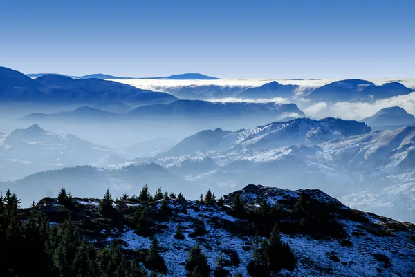 An epic ocean of clouds and fog in the winter mountains landscape, aerial view. Huge white clouds come in waves over the foggy valleys, mountain peaks rise over like islands. Dramatic overcast sky.