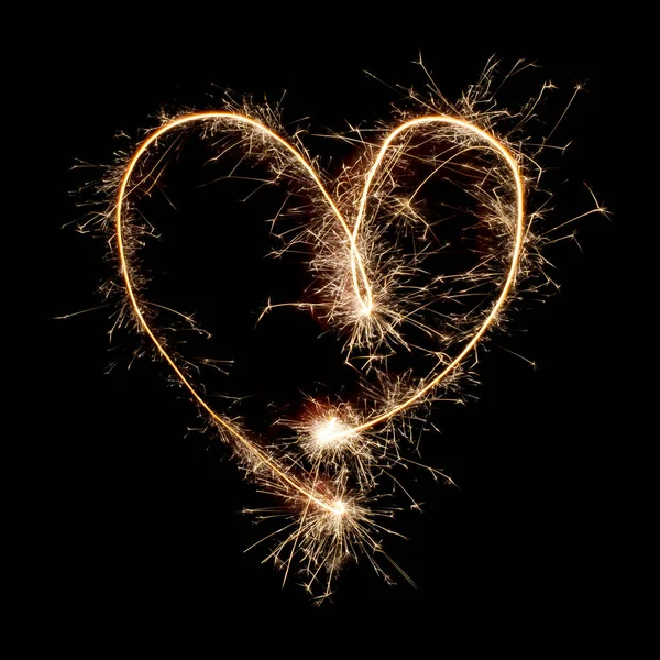Sparkling burning creative symbol heart isolated on black background. Beautiful glowing golden overlay object for design of holiday greeting card. Creative symbol heart written with burning sparklers