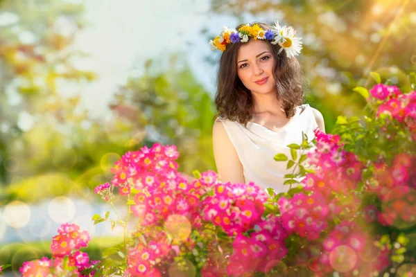 Fairy tale image art photo. Outdoor close up portrait of young beautiful happy smiling fantasy woman. Young goddess enjoys spring nature in bright sunlight and many pink roses.