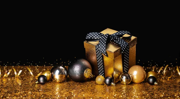stock image Congratulation Merry Christmas and Happy New Year. Golden box with a gift and Christmas balls on a black and gold background