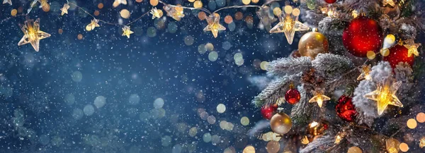 Mavi bir gecede takı taşıyan Noel ağacı - köknar dalları üzerindeki süslemeler parlak ve çözülmüş ışıklar ve soyut bir arkaplanda kar taneleri