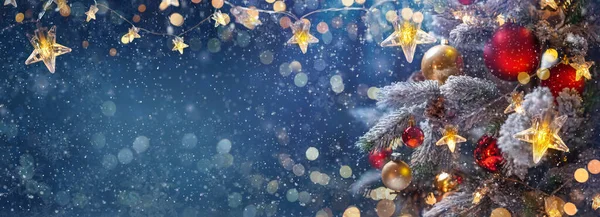 Mavi bir gecede takı taşıyan Noel ağacı - köknar dalları üzerindeki süslemeler parlak ve çözülmüş ışıklar ve soyut bir arkaplanda kar taneleri