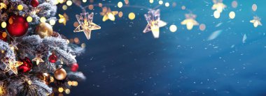 Mavi bir gecede takı taşıyan Noel ağacı - köknar dalları üzerindeki süslemeler parlak ve çözülmüş ışıklar ve soyut bir arkaplanda kar taneleri