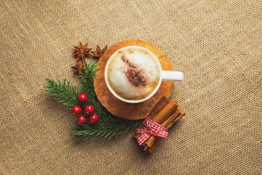 Beyaz bir fincanda kapuçino kahvesi. Bakır bir fincan üzerinde. Bir masa örtüsünün ve Noel süslemelerinin arka planında.