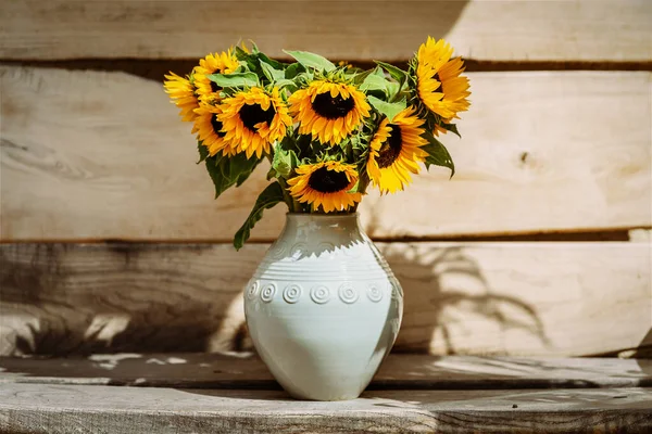 Bouquet of sunflowers in a ceramic white vase on a wooden background
