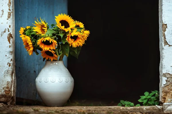 a bouquet of sunflowers in a white vase against the background of an old rustic door