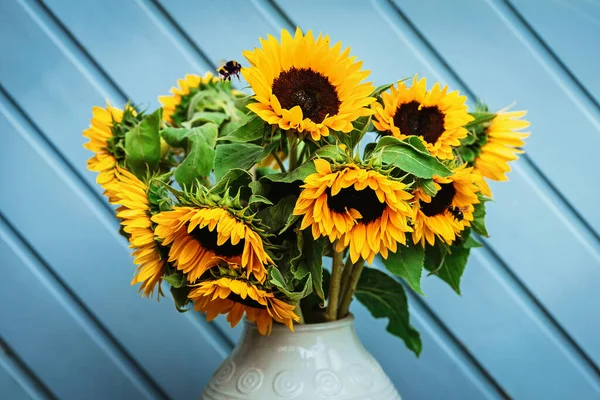 Bouquet of sunflowers in a white vase against the background of an old blue door