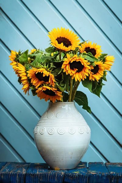 Bouquet of sunflowers in a white vase against the background of an old blue door