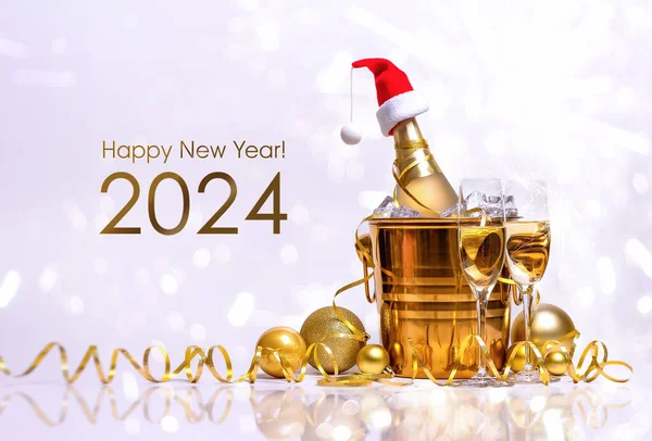 Kırmızı Noel Baba şapkalı bir şişe şampanya, altın kovada buz ve beyaz arka planda iki bardak..
