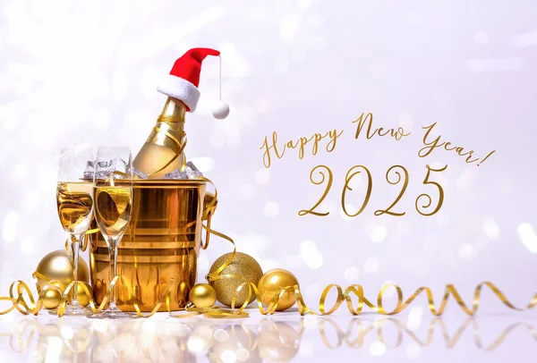 Kırmızı Noel Baba şapkalı bir şişe şampanya, altın kovada buz ve beyaz arka planda iki bardak..