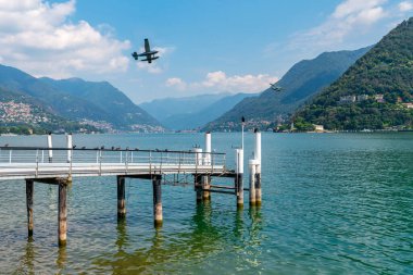 Como, İtalya. Rıhtım manzarası, göl ve dağların üzerinde uçan turist uçakları.