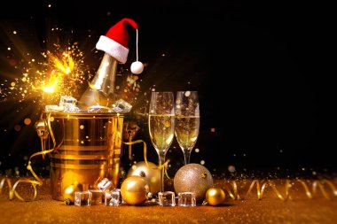 Altın kovada bir şişe şampanya, buzlu ve iki bardak şampanyayla Noel süslemelerinde siyah arka planda..