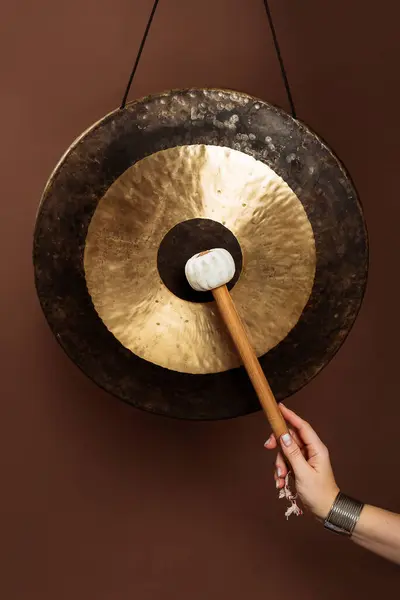 Stock image Tibetan bronze gong and a female hand with a mallet on a brown background