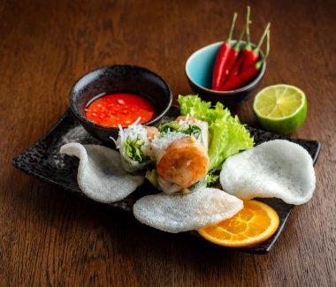 Asya mutfağı. Karides ve pirinç rulosu, pirinç ekmeği ve acı sos siyah seramik tabaklarda.