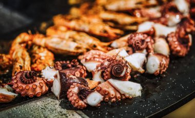 Büyük bir ızgarada karides, ahtapot ve sosis pişiriyorum.