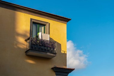Mavi gökyüzüne karşı balkonu olan sarı bir İtalyan evinin parçası.