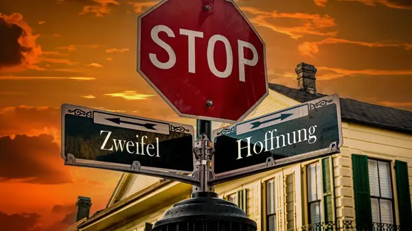 stock image An image with a signpost pointing in two different directions in German. One direction points to hope, the other points to doubt.