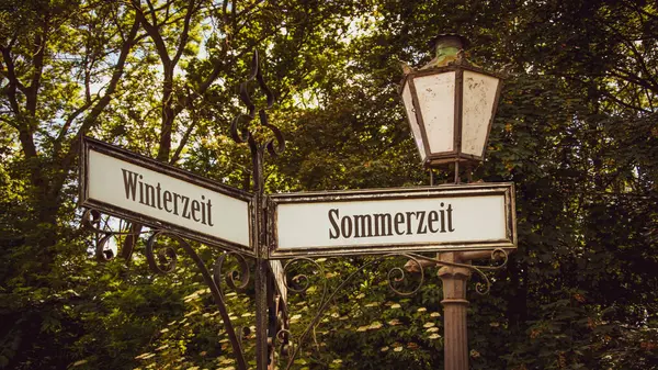 stock image An image with a signpost pointing in two different directions in German. One direction shows Daylight Saving Time, the other shows Winter Time.