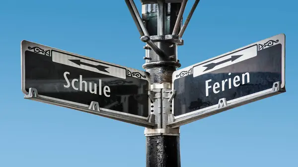 stock image An image with a signpost pointing in two different directions in German. One direction points to holidays, the other points to school.