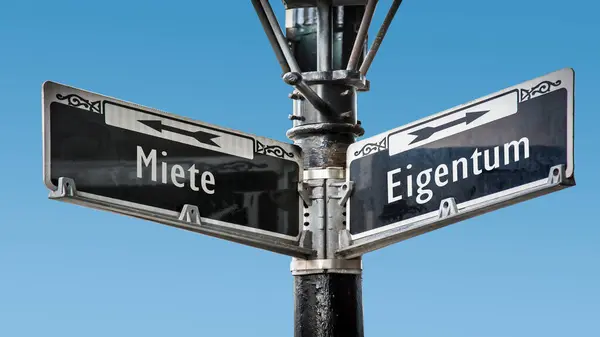 stock image An image with a signpost pointing in two different directions in German. One direction points to ownership, the other points to rent.