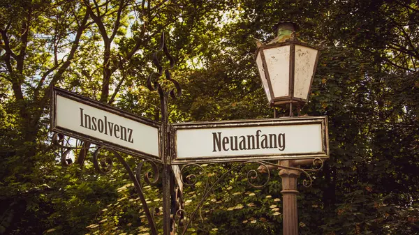 stock image An image with a signpost pointing in two different directions in German. One direction points to a fresh start, the other points to bankruptcy.