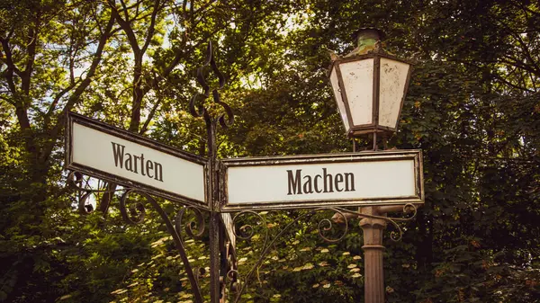 stock image An image with a signpost pointing in two different directions in German. One direction is to do, the other is to wait.