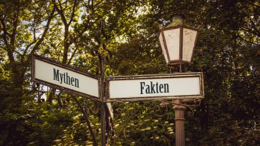 An image with a signpost pointing in two different directions in German. One direction points to facts, the other points to myths. clipart