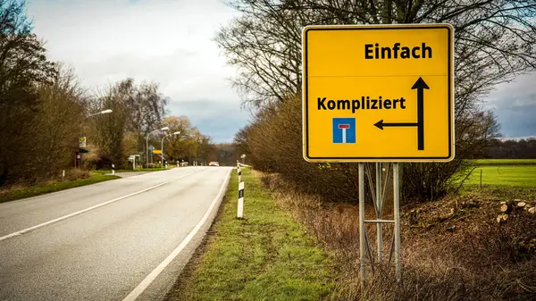 Stock image An image with a signpost pointing in two different directions in German. One direction points to Simple, the other points to Complicated.