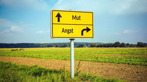 stock image An image with a signpost pointing in two different directions in German. One direction points to courage, the other points to fear.